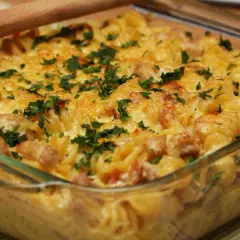 Zapiekanka makaronowa z kurczakiem i serem, posypana natką pietruszki, w szklanym naczyniu.