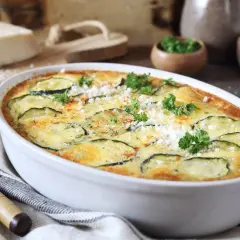 Zapiekanka z cukinii w białym naczyniu, ozdobiona natką pietruszki i parmezanem.