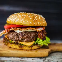 Soczysty domowy burger z bekonem, serem, pomidorem i sałatą na desce.