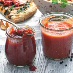 Dwa słoiki domowego sosu pomidorowego do pizzy, jeden z łyżką.