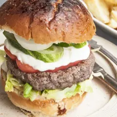 Domowy hamburger z soczystym kotletem, warzywami i frytkami w tle.