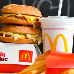 Dwa burgery Big Mac, frytki i napój McDonald's na tle tablicy.