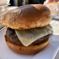 Hamburger z serem na białym talerzu, obok koszyka na frytki.