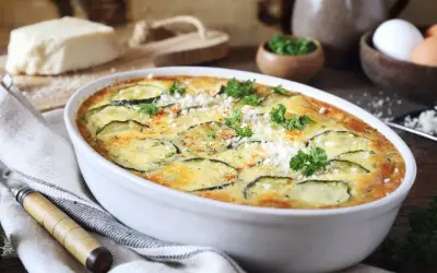 Zapiekanka z cukinii w białym naczyniu, ozdobiona natką pietruszki i parmezanem.