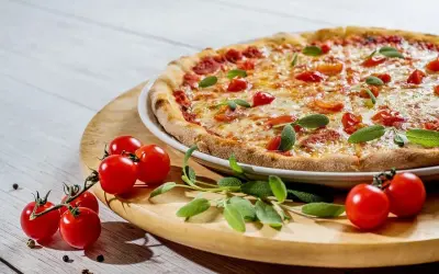 Pizza z pomidorkami koktajlowymi i bazylią na drewnianej desce.