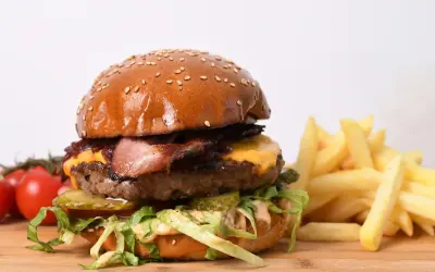 Apetyczny burger wołowy z bekonem, serem, warzywami i frytkami na desce.
