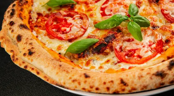 Zbliżenie na domową pizzę z pomidorami, serem i bazylią, z przypieczonym brzegiem.