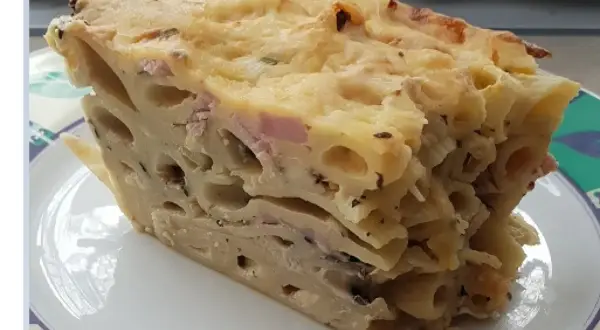 Kawałek zapiekanki makaronowej z serem i szynką na talerzu.