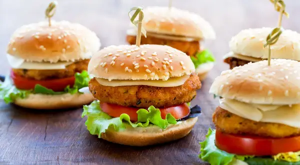 Kilka mini burgerów z serem, pomidorem i sałatą na drewnianym tle.