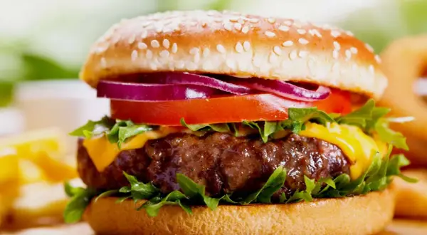 Soczysty burger z serem, pomidorem, czerwoną cebulą i sałatą na bułce z sezamem.