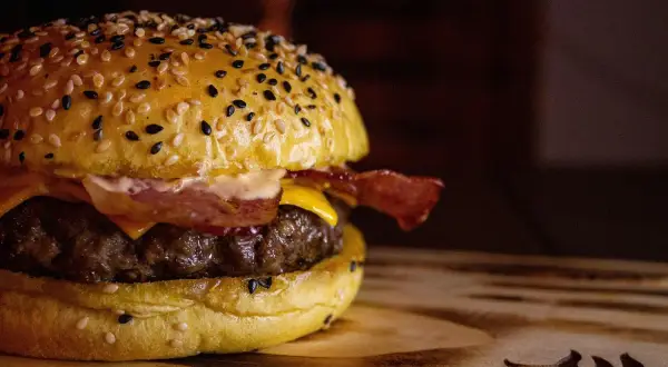 Apetyczny burger z sezamową bułką, serem, bekonem i soczystym mięsem na drewnianej desce.