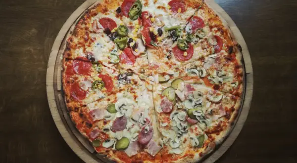 Pizza podzielona na cztery części z różnymi dodatkami: salami, jalapeno, kukurydza, pieczarki, szynka i ogórek.