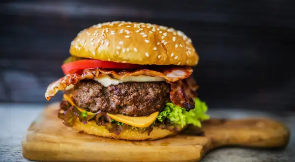 Soczysty domowy burger z bekonem, serem, pomidorem i sałatą na desce.