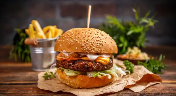 Soczysty burger z serem i bekonem, podany z frytkami i surówką na drewnianym stole.