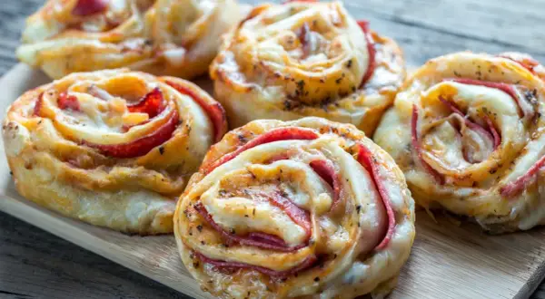 Roladki z ciasta na pizzę z serem i wędliną, ułożone na desce.