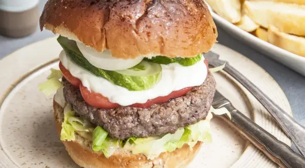 Domowy hamburger z soczystym kotletem, warzywami i frytkami w tle.