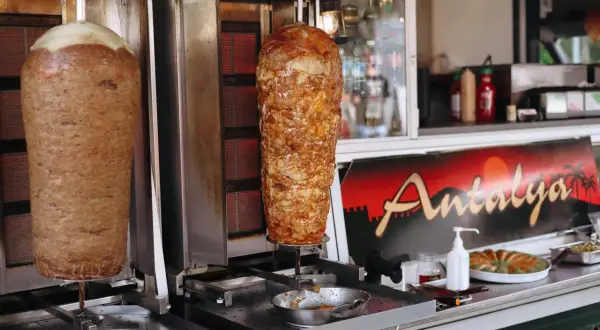 Dwa pionowe rożna z mięsem do kebaba na tle budki z napisem "Antalya".