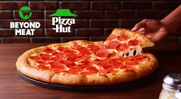Pizza pepperoni z ciągnącym się serem, podnoszona przez rękę. Logo Beyond Meat i Pizza Hut w tle.