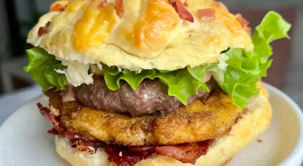 Domowy hamburger z serem, bekonem, sałatą i panierowanym kotletem na talerzu.